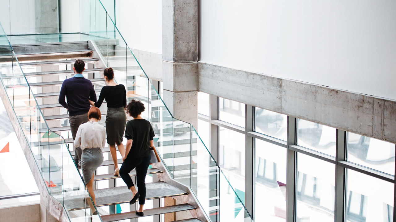 A group of professionals walks up an open office staircase
