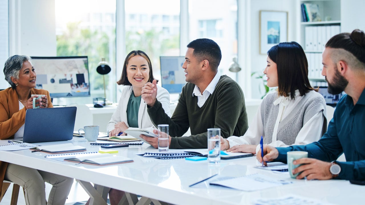 A group of professionals meet around a brightly lit conference room table